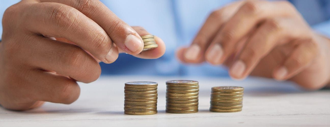 Mains empilant des pièces de monnaie, symbolisant la réduction des cotisations patronales.