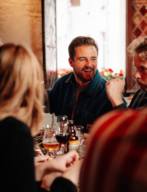Charlie Gordower aan tafel in een restaurant in Brussel, omringd door gasten tijdens een gezellige maaltijd